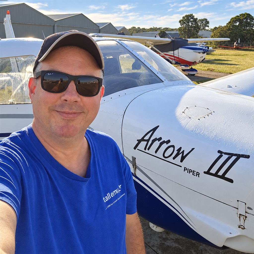 Mike Nash, founder and CEO of Tall Emu, beside a Piper Arrow aircraft, wearing a blue Tall Emu shirt, cap and sunglasses
